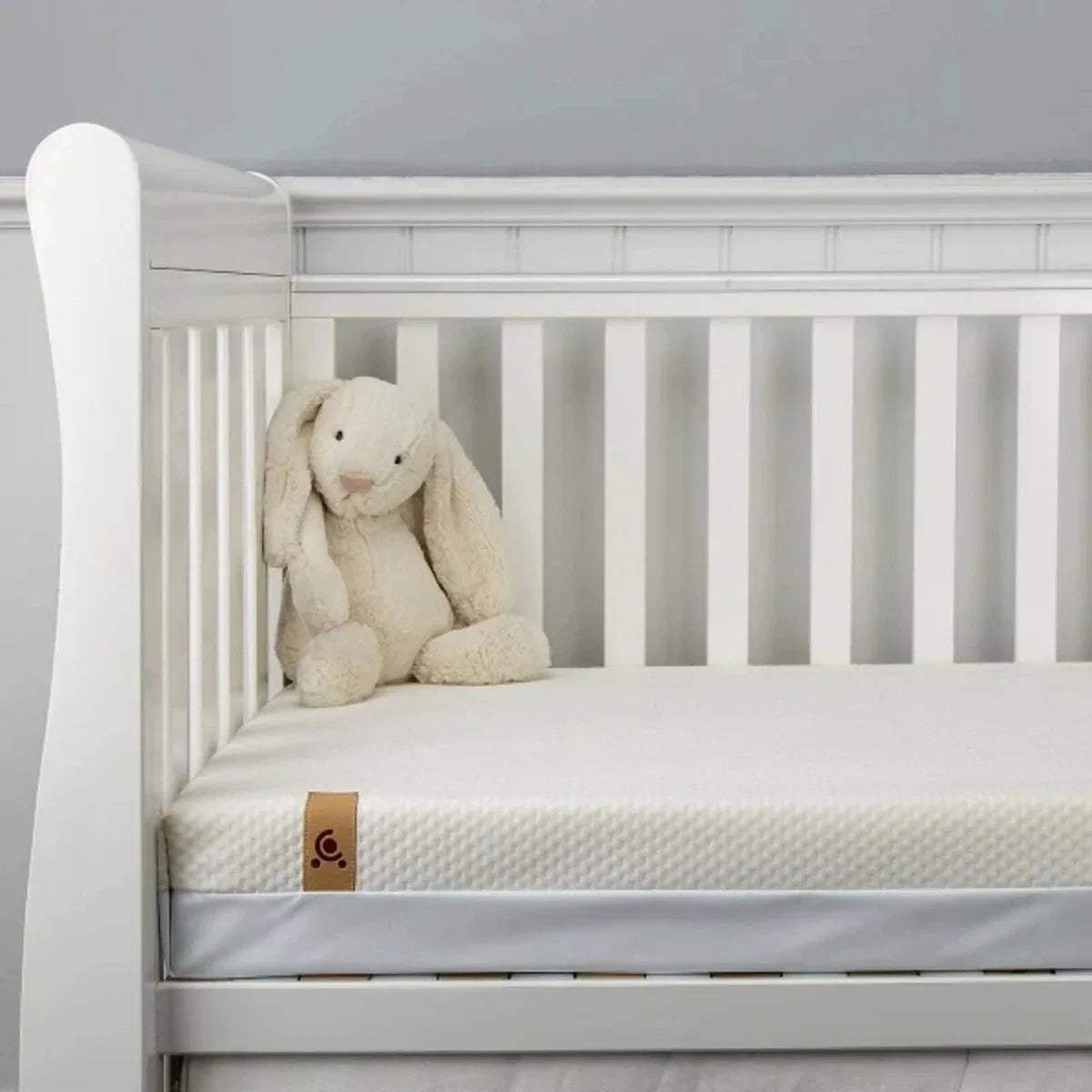 White cot mattress with coil springs shown on a slatted bed, with teddy bear