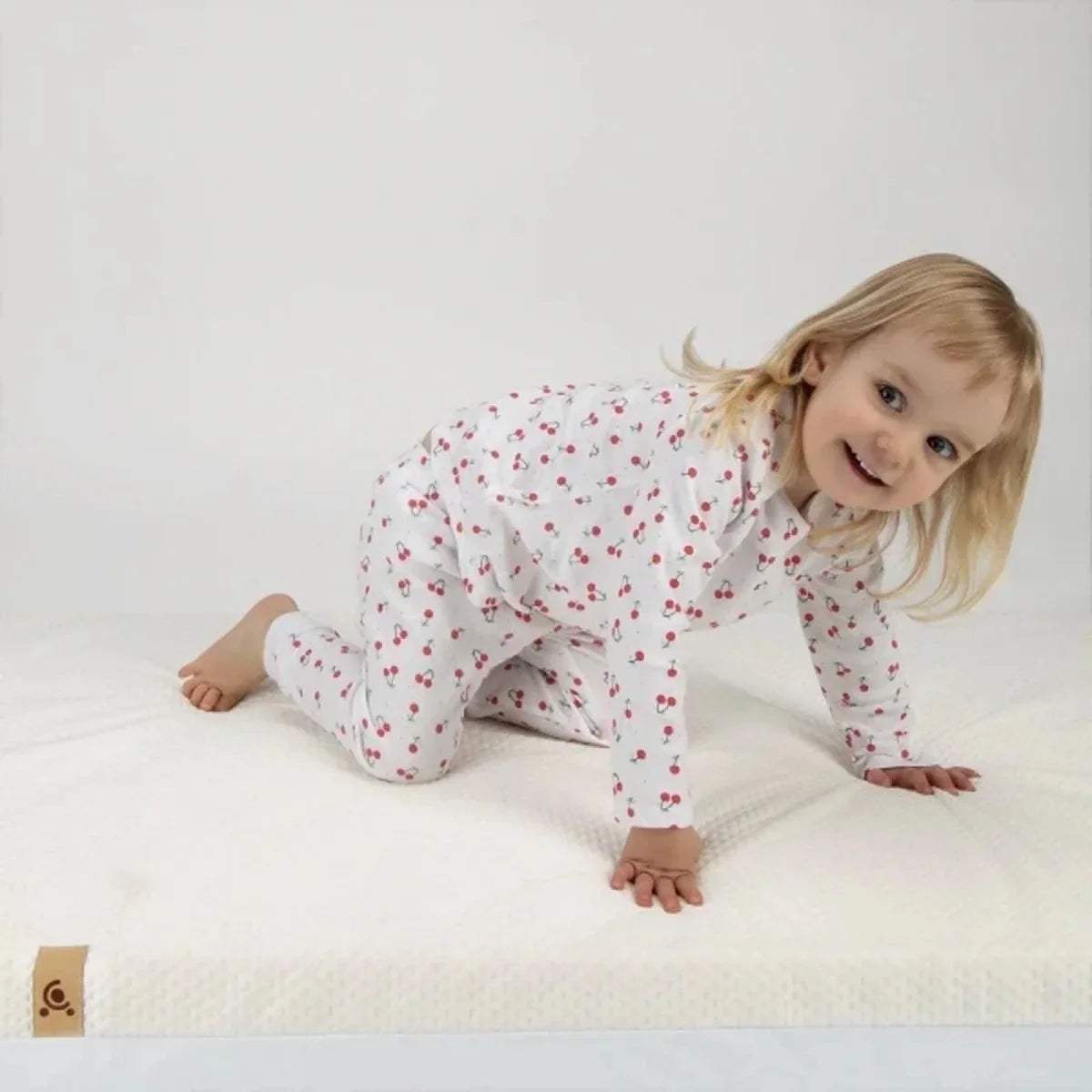 White cot mattress with textured cover, shown with a child lying on top