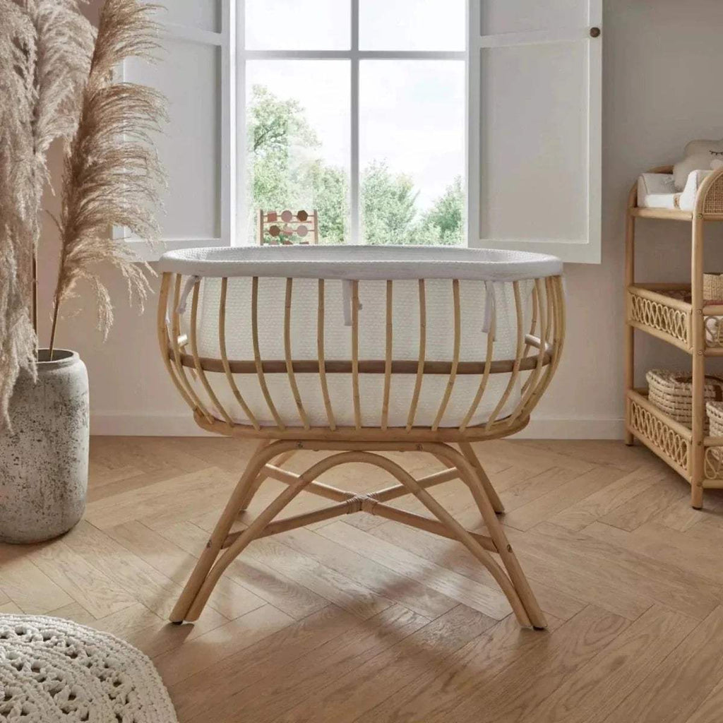 Natural rattan baby crib with white padded rim, woven sides, and curved rocking legs