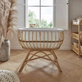 Natural rattan baby crib with white padded rim, woven sides, and curved rocking legs