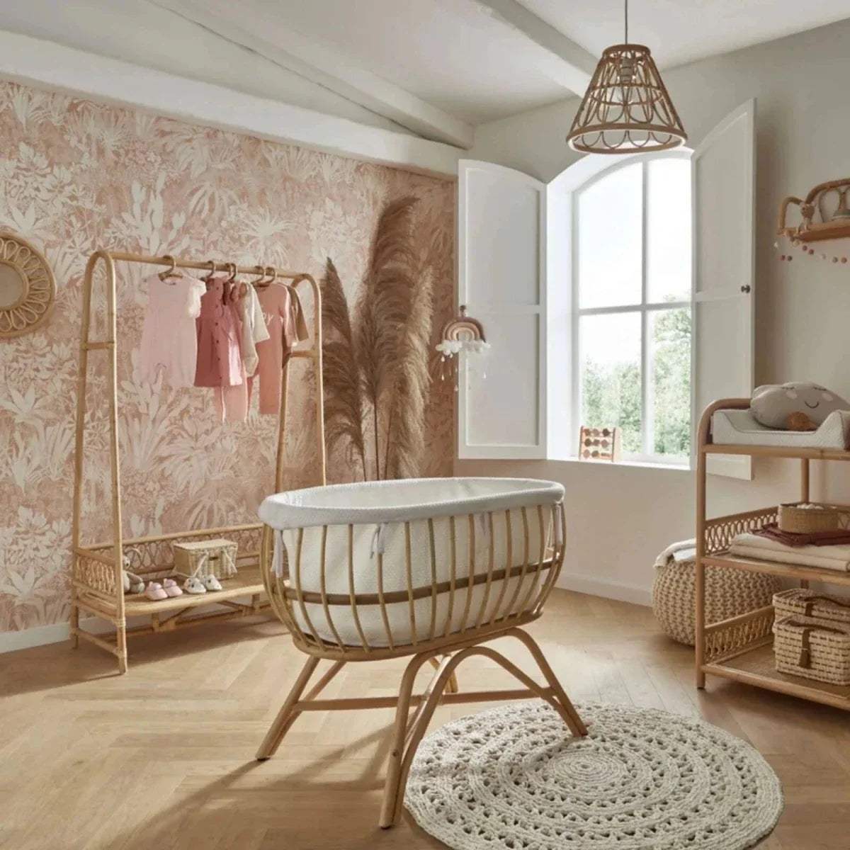 Natural rattan baby crib with white padded rim, woven sides, and wooden stand