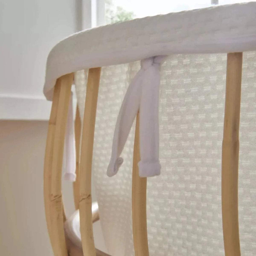Close-up of natural rattan crib rails with white padded fabric and hanging ties