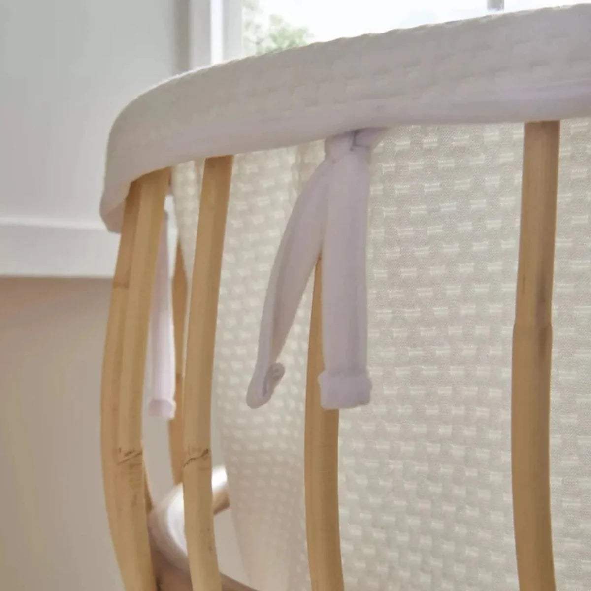 Close-up of natural rattan crib rails with white padded fabric and hanging ties