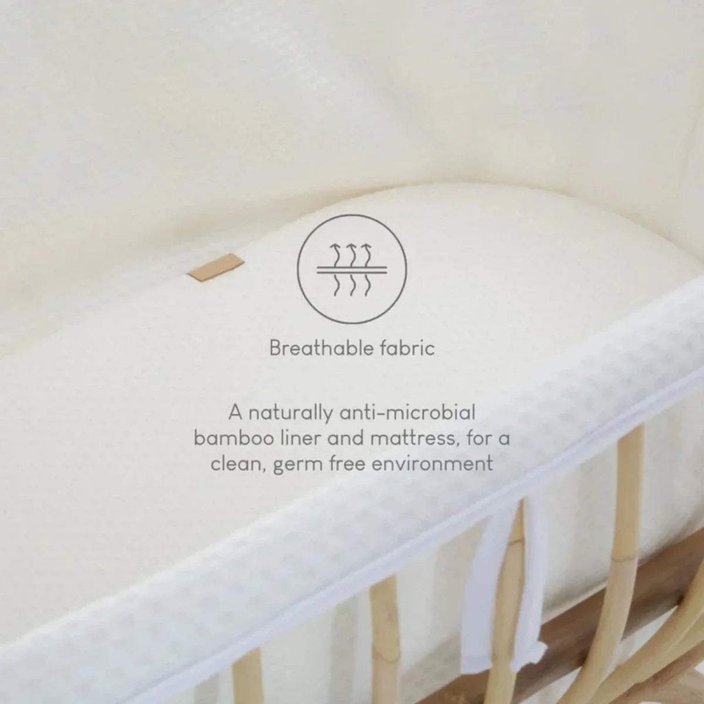White breathable liner and mattress inside natural rattan baby crib with fabric edges