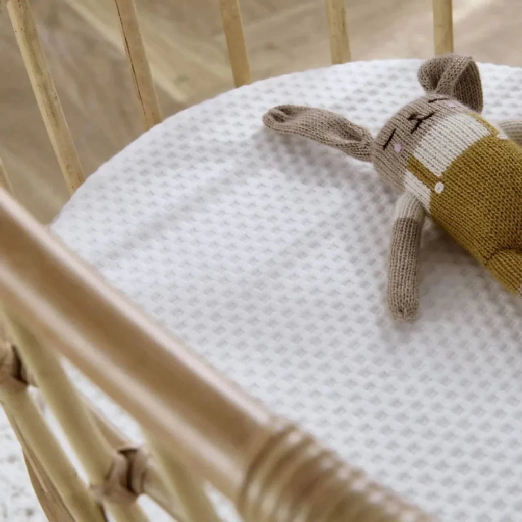 Rattan crib mattress with white textured sheet and small plush toy on top