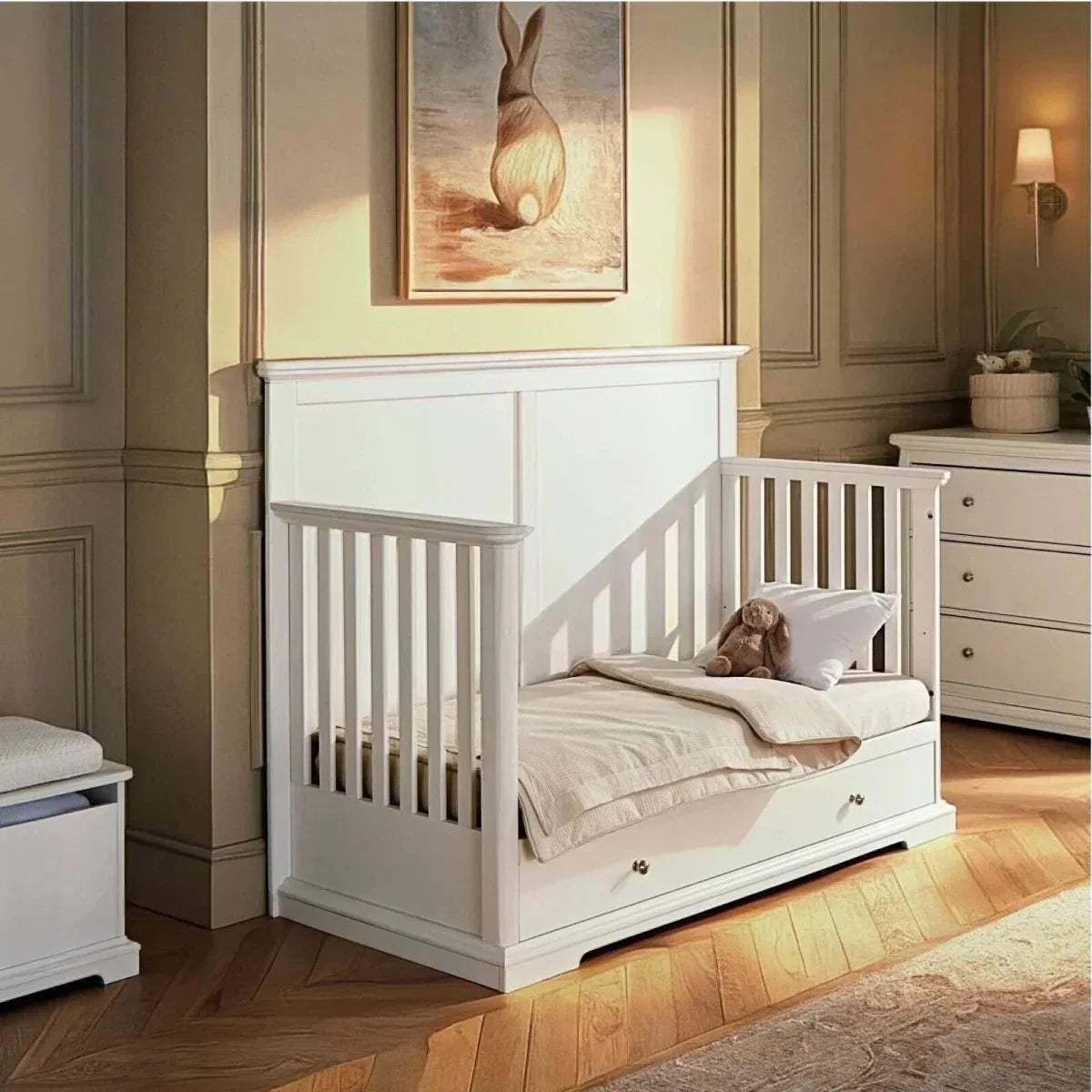 White cot bed with slatted sides and open front, ready for a mattress