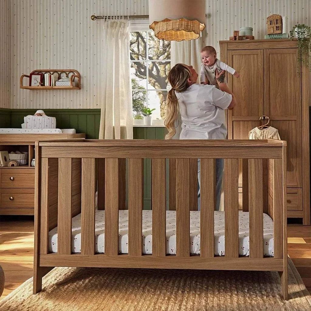 Oak cot bed with slatted sides and end rails, shown in use