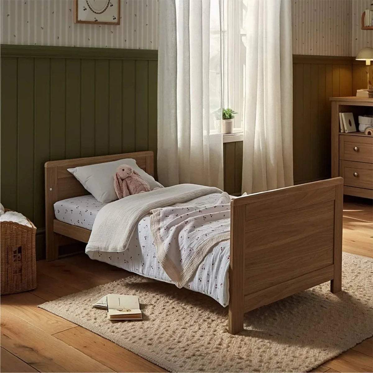 Oak cot bed with slatted side rails and fitted light-colored bedding