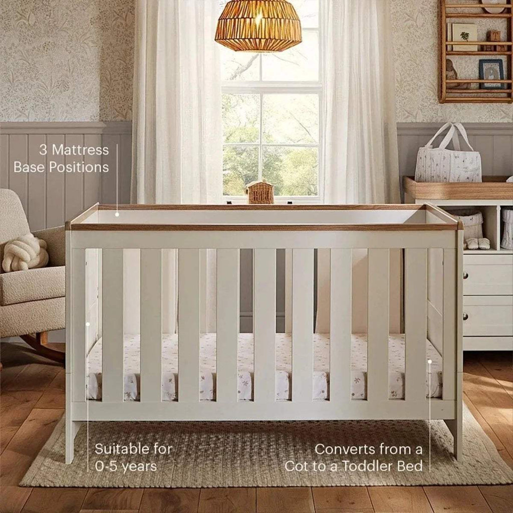 White cot bed with slatted sides and oak-toned top rail, front end visible