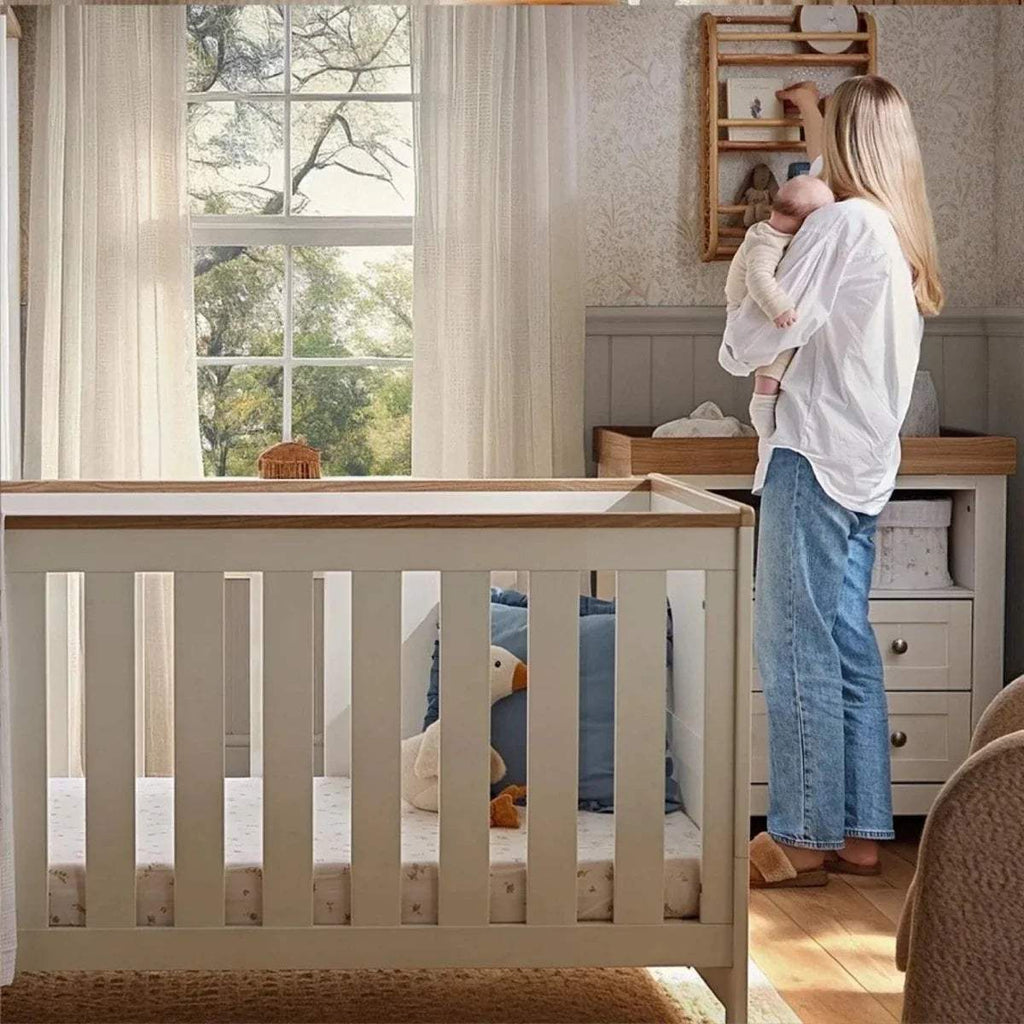 White cot bed with slatted sides and oak-toned top rail in a nursery room