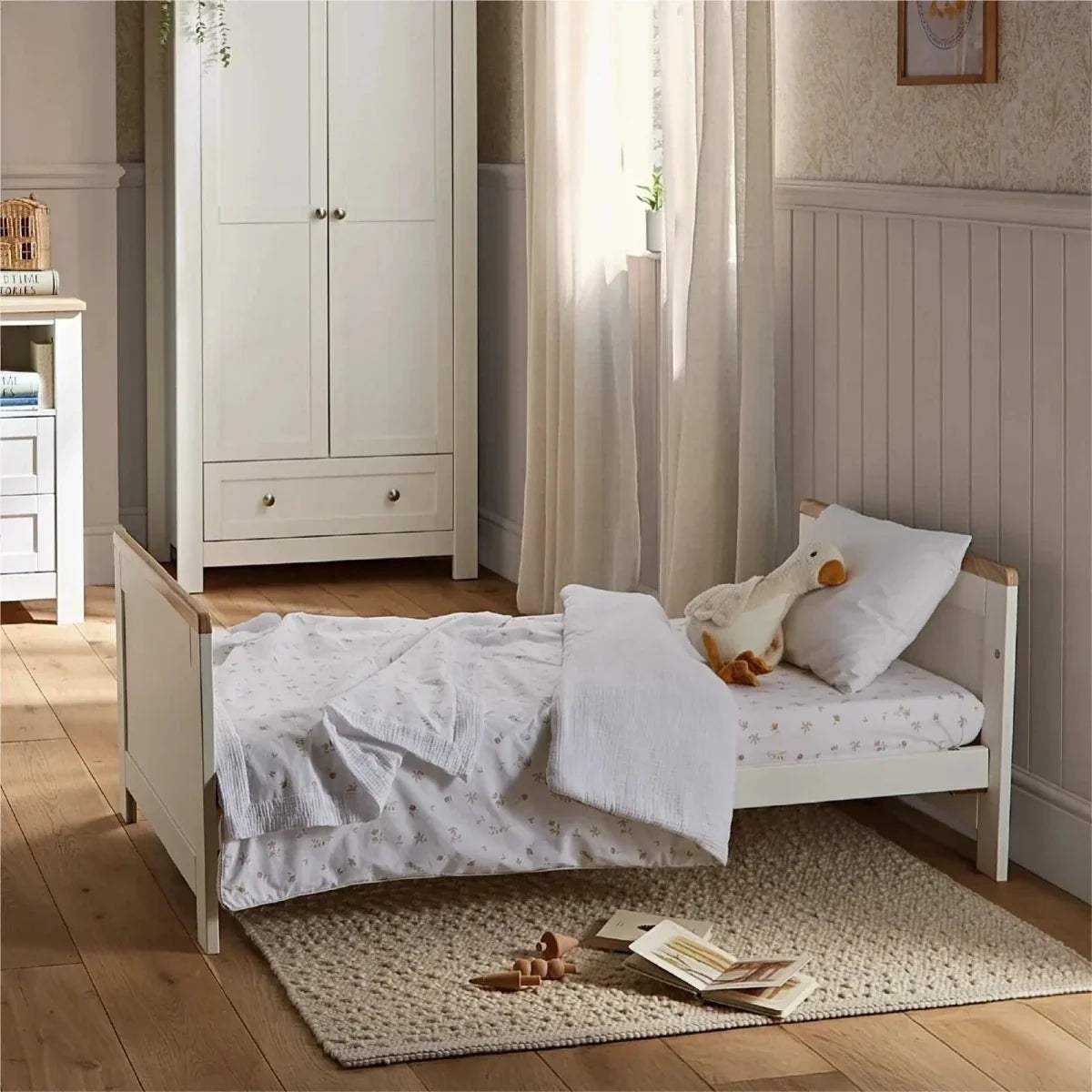 White daybed-style nursery bed with side rails and white bedding on rug