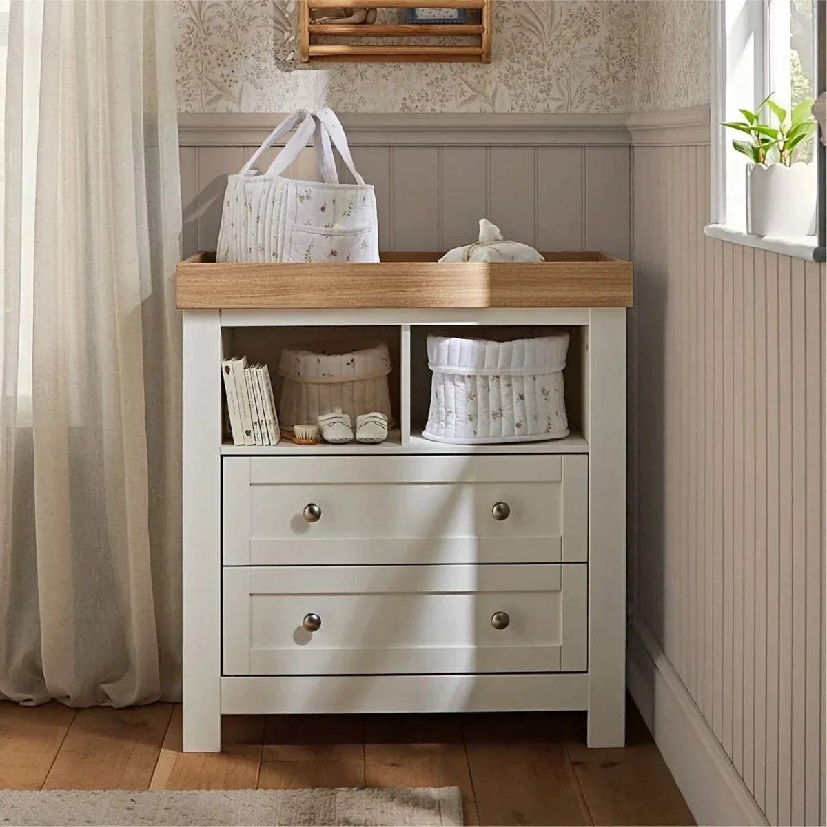 White nursery dresser with wood top, open shelf, drawers, and storage compartments