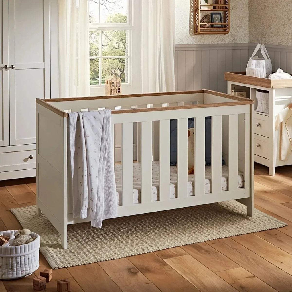 White nursery cot with slatted panels and light wood headboard in corner