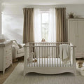 White nursery crib with spindle sides, curved base, and beige blanket
