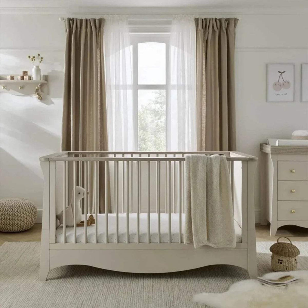 White nursery crib with protective rail, beige draped blanket and bedding