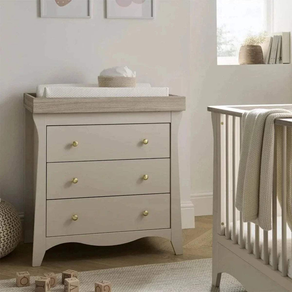 White nursery dresser with three drawers and brass knobs, crib rail nearby