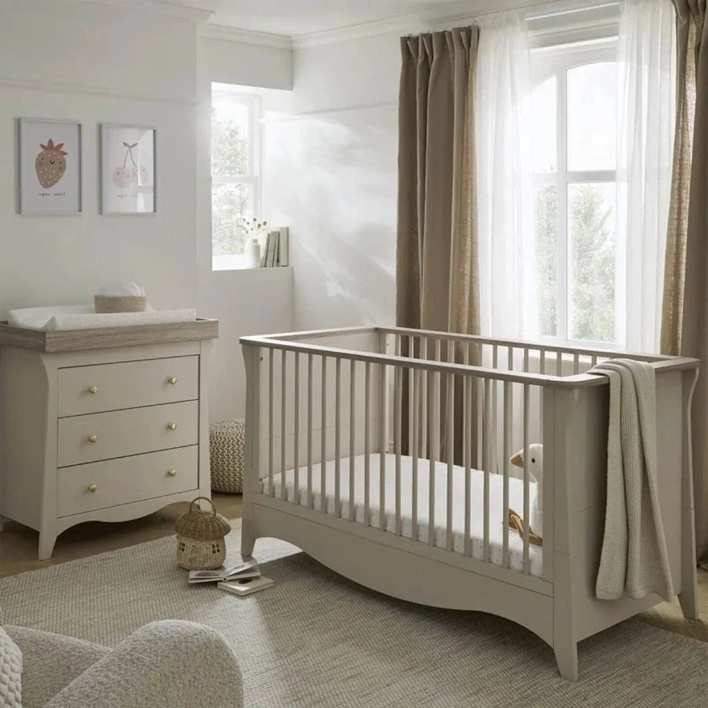 White nursery crib with vertical slats and matching 3-drawer dresser, styled with soft textiles