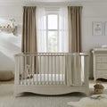 White Clara cot bed with vertical slatted sides and draped neutral blanket