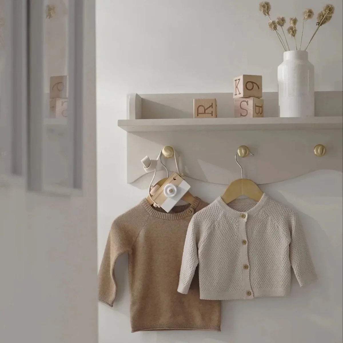 Nursery wall shelf with scalloped front, styled with knit baby sweaters on hangers