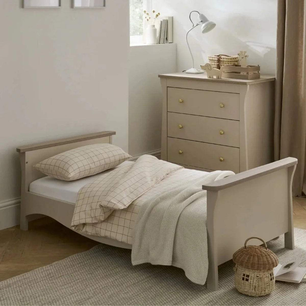 Cream toddler bed with paneled sides, grid pillows, and a light throw blanket