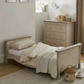 Cream toddler bed with paneled sides, grid pillows, and a light throw blanket