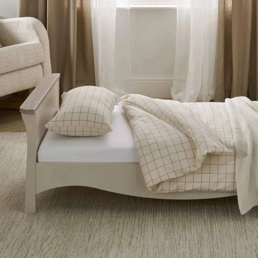 Cream toddler bed with grid pillow set and draped light throw over the mattress