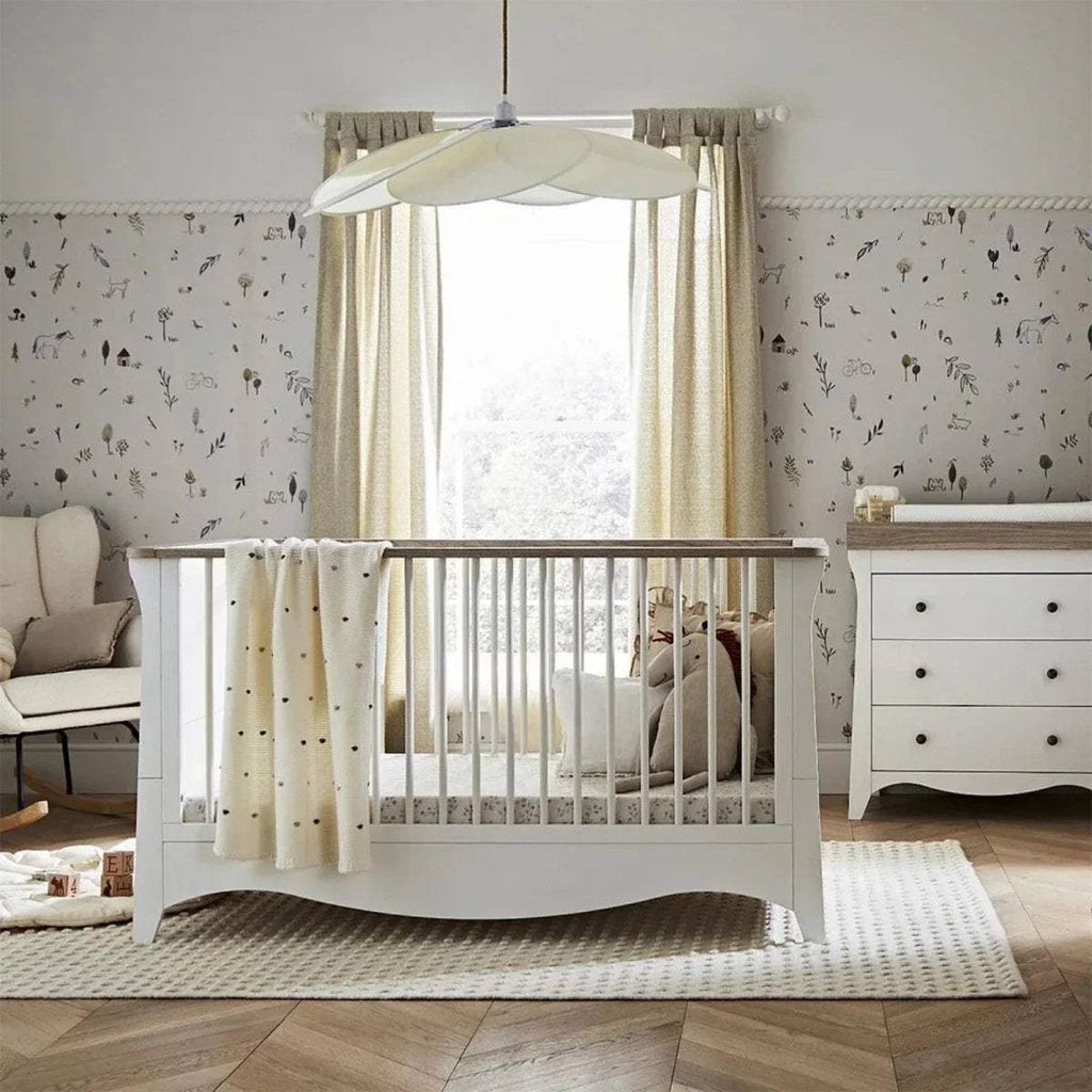 White nursery crib with rounded posts, canopy frame, and beige fabric curtains
