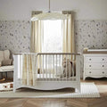 White nursery crib with rounded posts, canopy frame, and beige fabric curtains