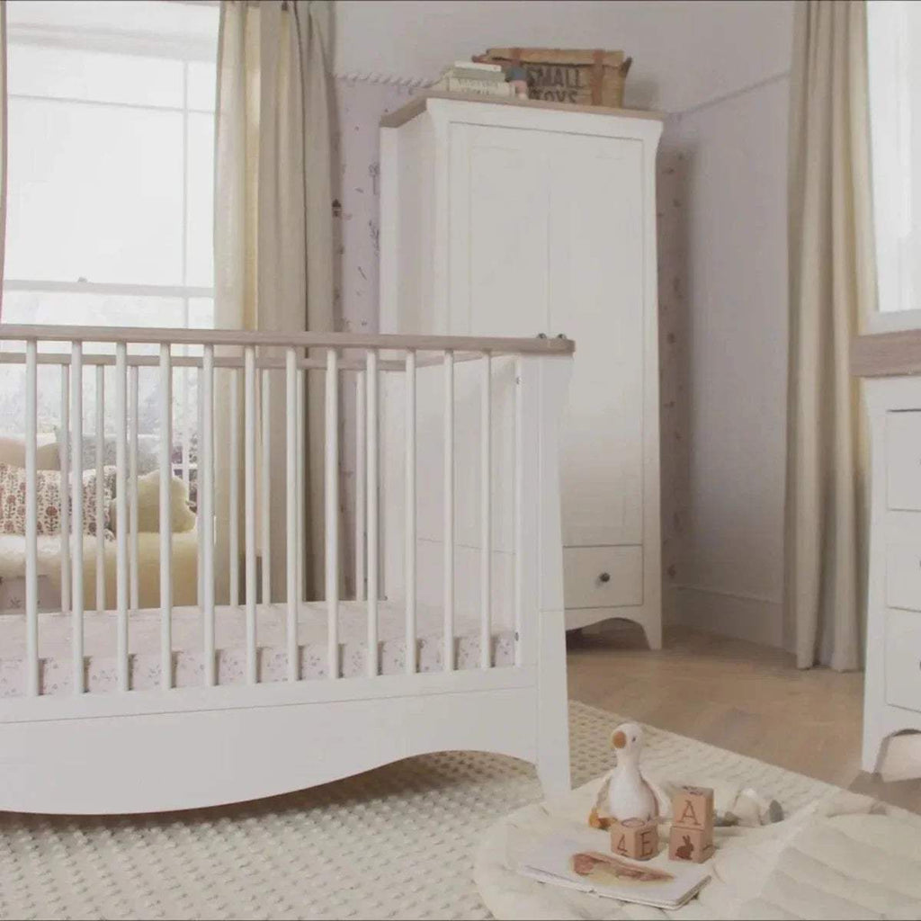White nursery crib with slat sides and a tall white dresser in the background