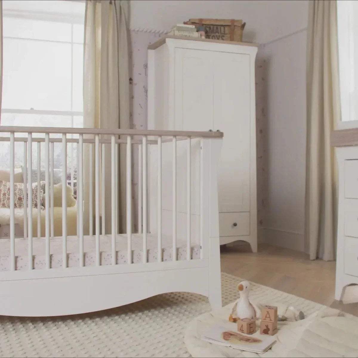 White nursery crib with slat sides and a tall white dresser in the background