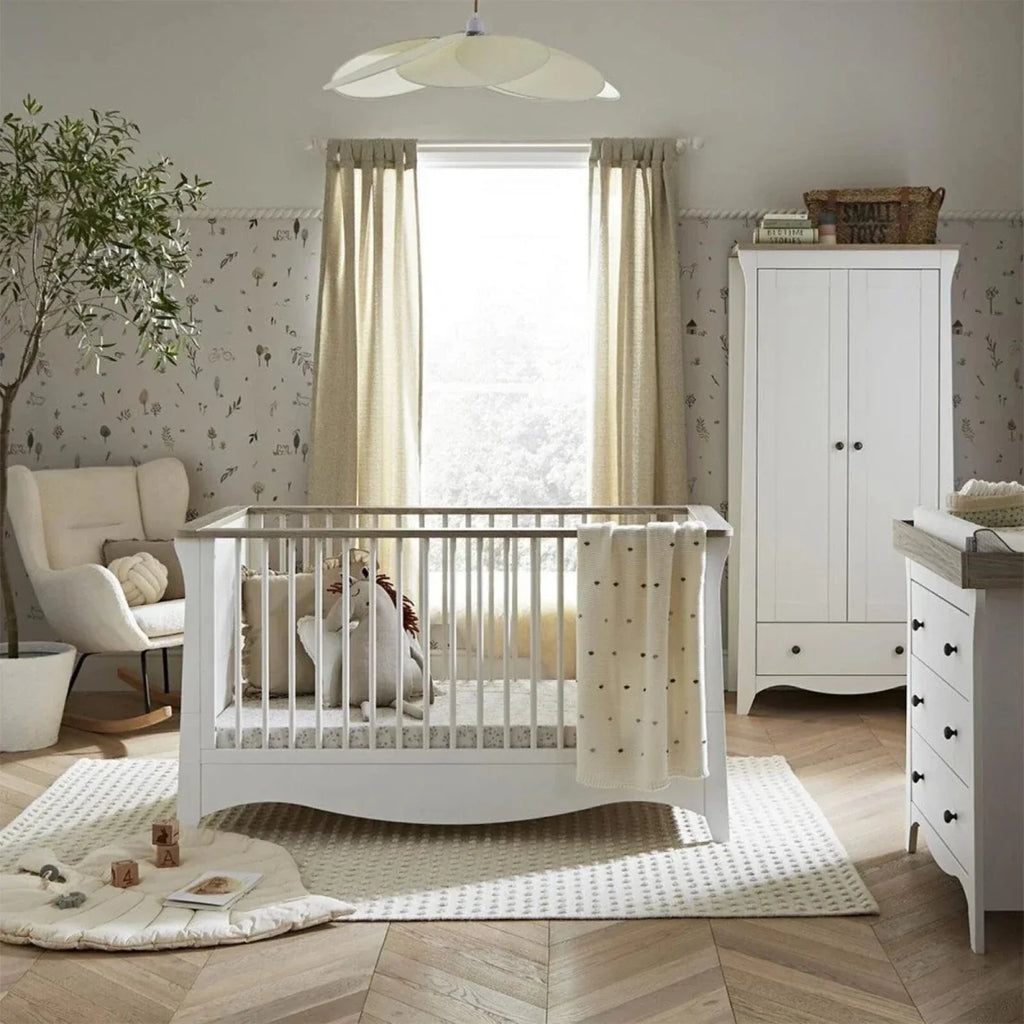 White nursery crib with vertical slats and ash-toned drawer cabinet behind.