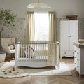 White nursery crib with vertical slats and ash-toned drawer cabinet behind.