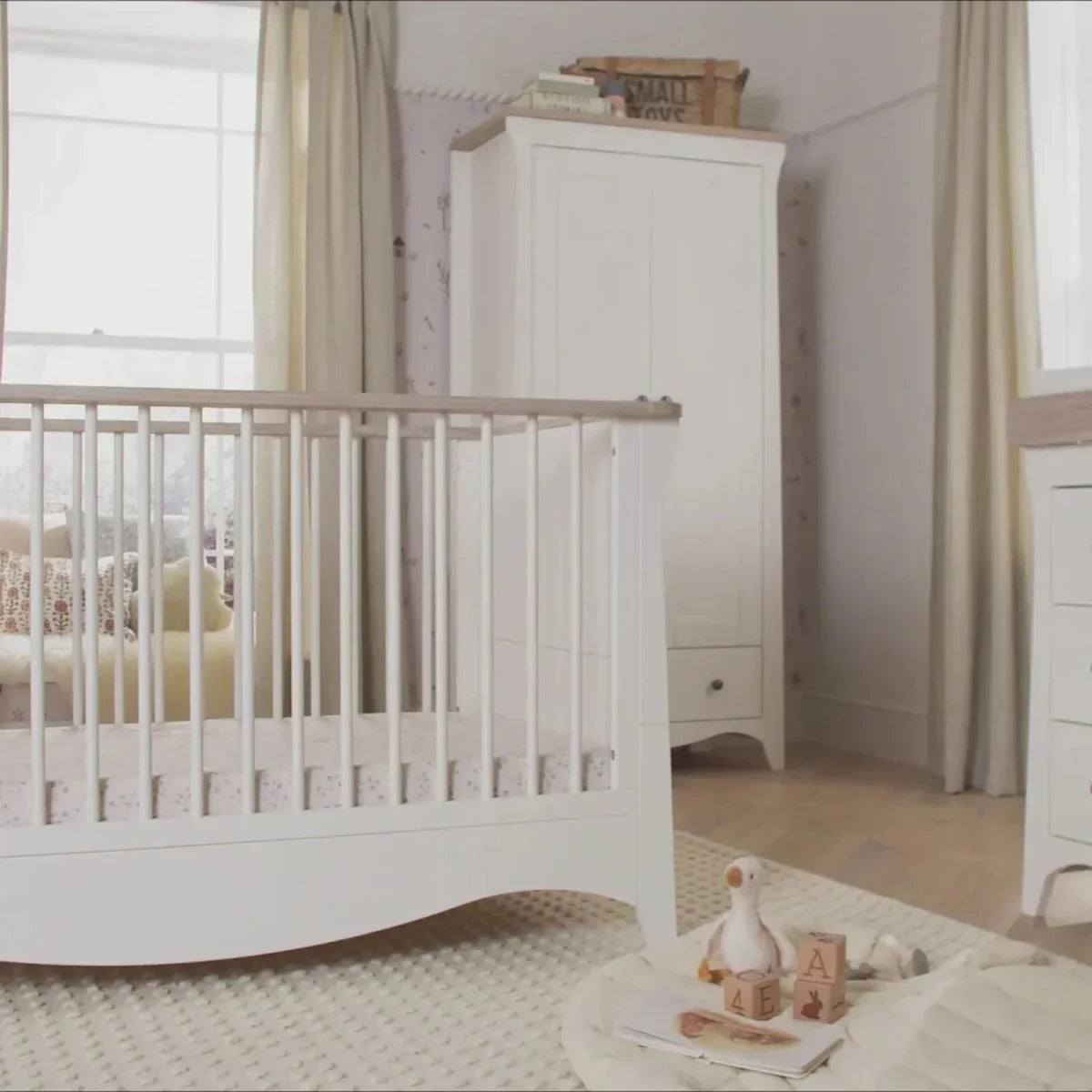 White nursery crib with curved base and open slats; tall storage cabinet with drawers.