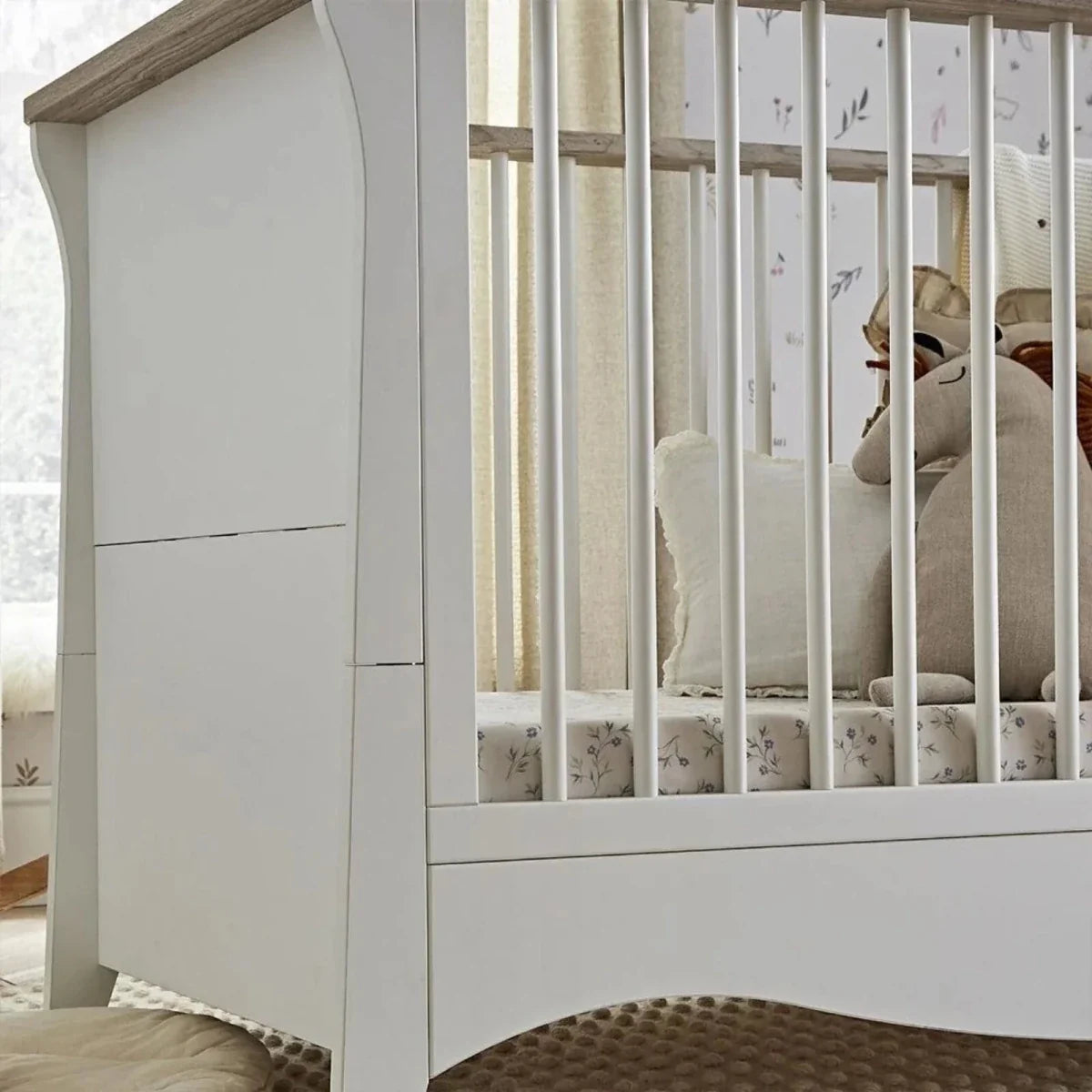 White nursery cabinet with ash-toned top panel and arched lower detail.