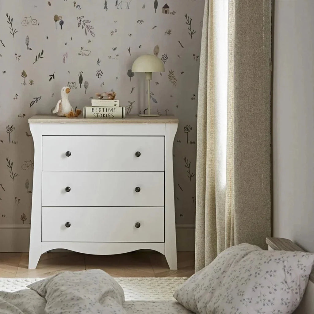White nursery dresser with three drawers, round knobs, and curved apron base.