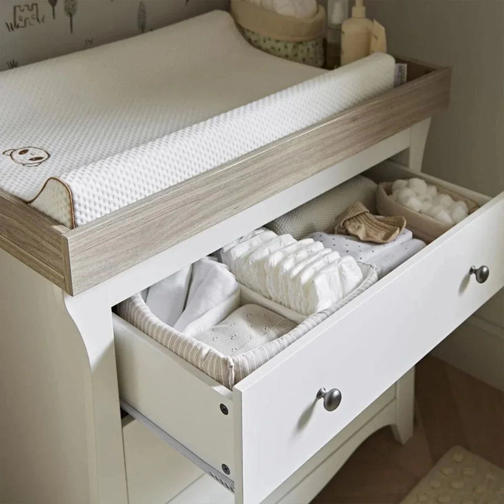 White nursery bed with ash side rail and pull-out drawer for folded bedding.
