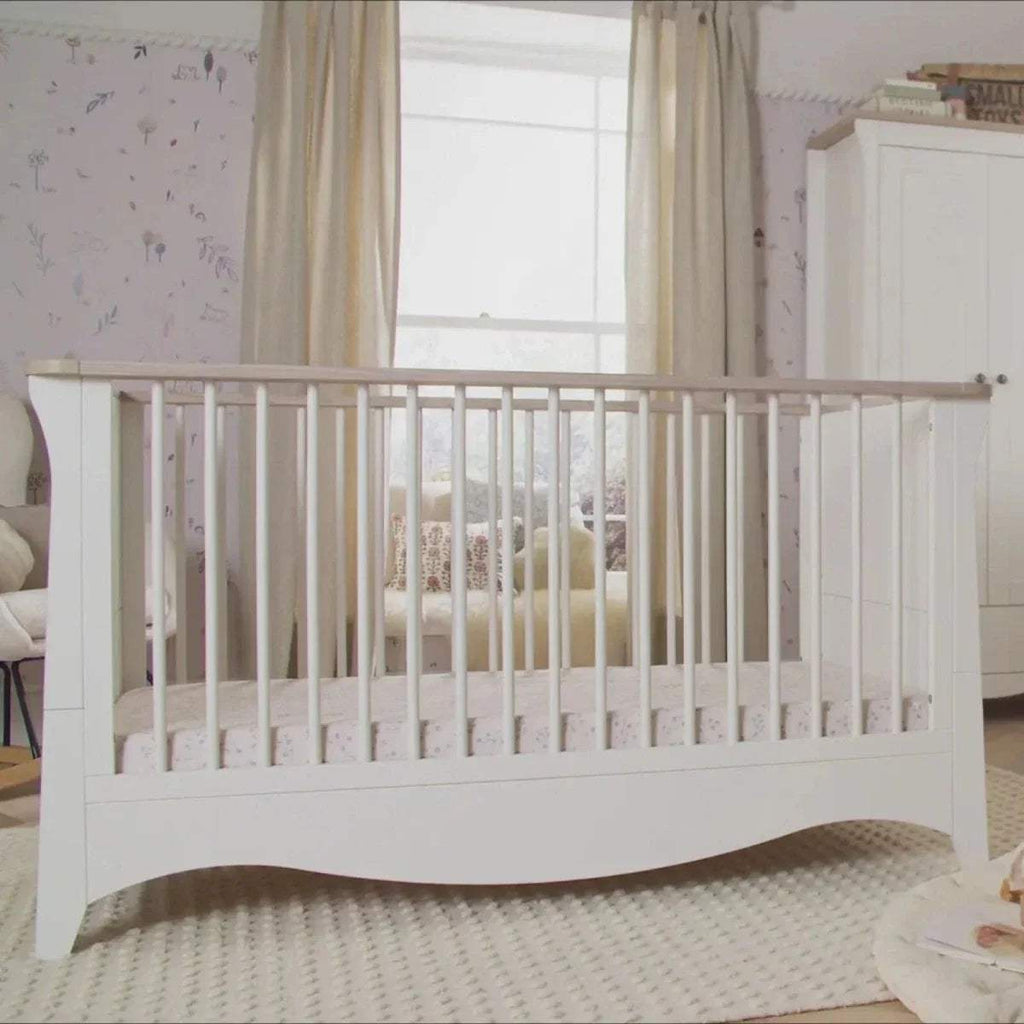 White cot bed with vertical bars, curved base, and light ash top rail