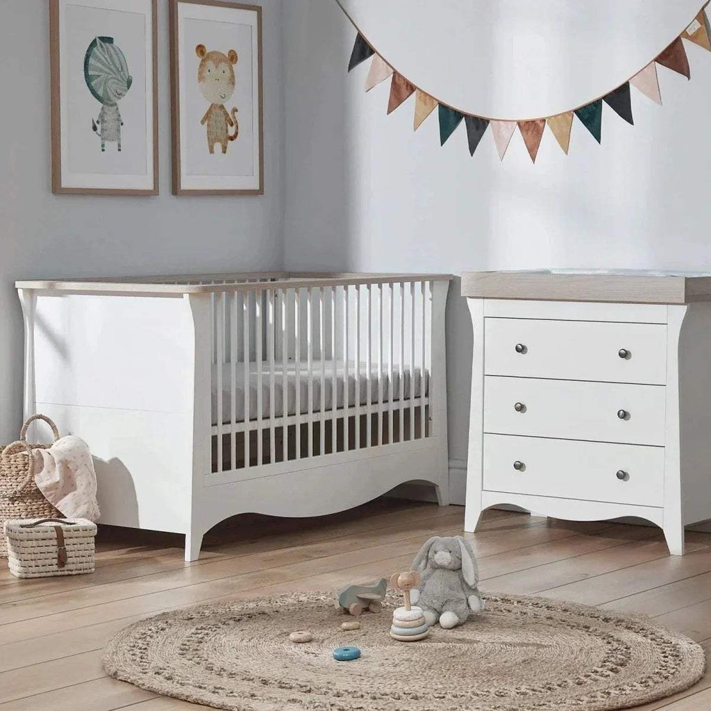 White cot bed with vertical slats and curved base, shown with padded mattress