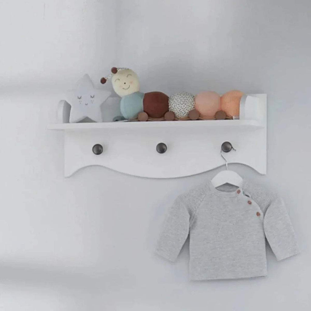 White wall shelf with top ledge, three knobs, and a hanging baby outfit