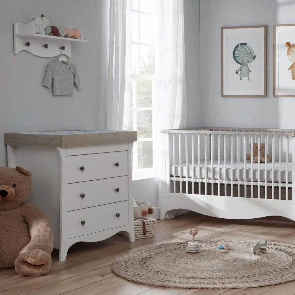 White wall shelf with ledge and hooks, styled with baby clothes and toys