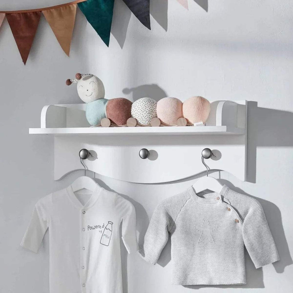 White wall shelf with ledge and three hooks holding baby tops