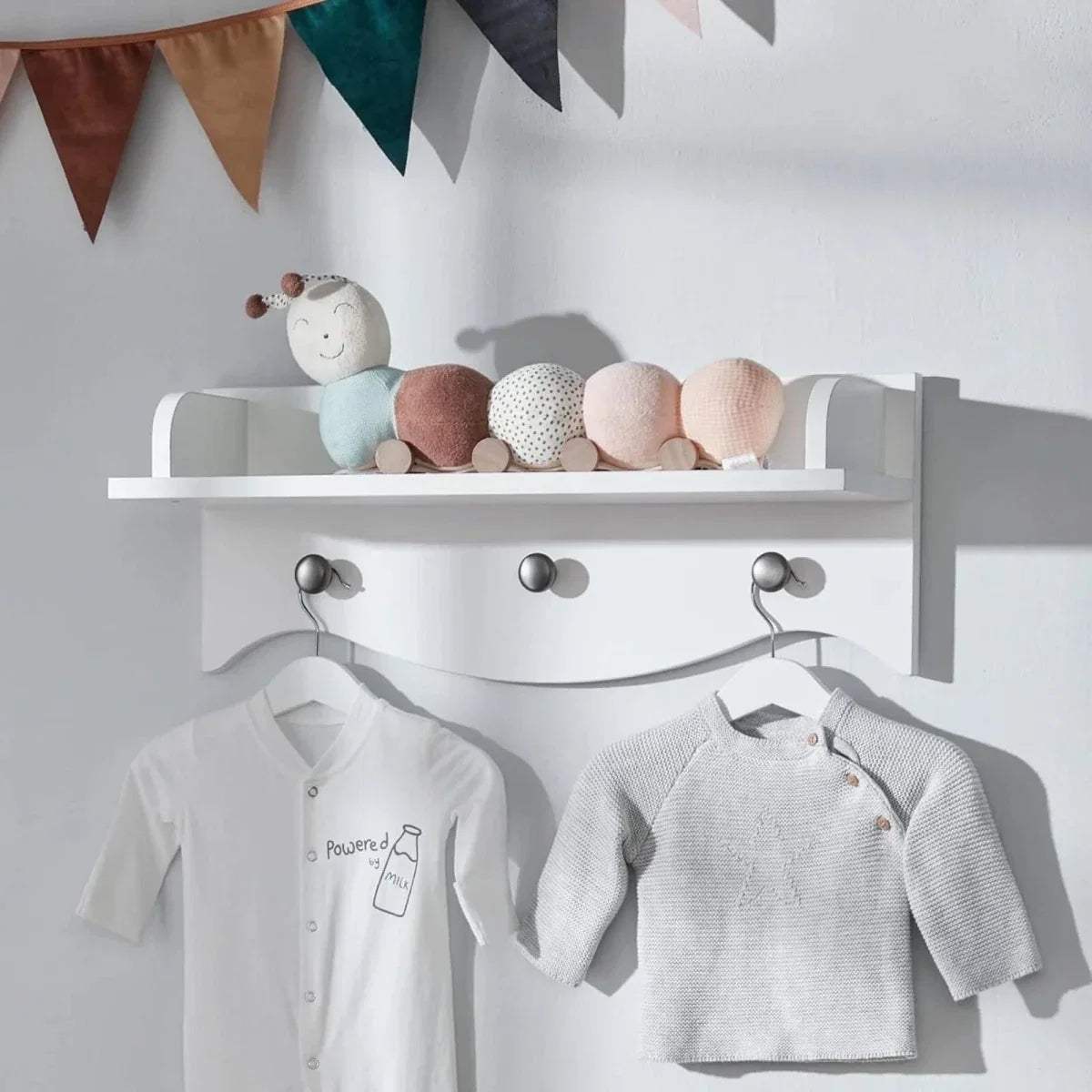 White wall shelf with ledge and three hooks holding baby tops