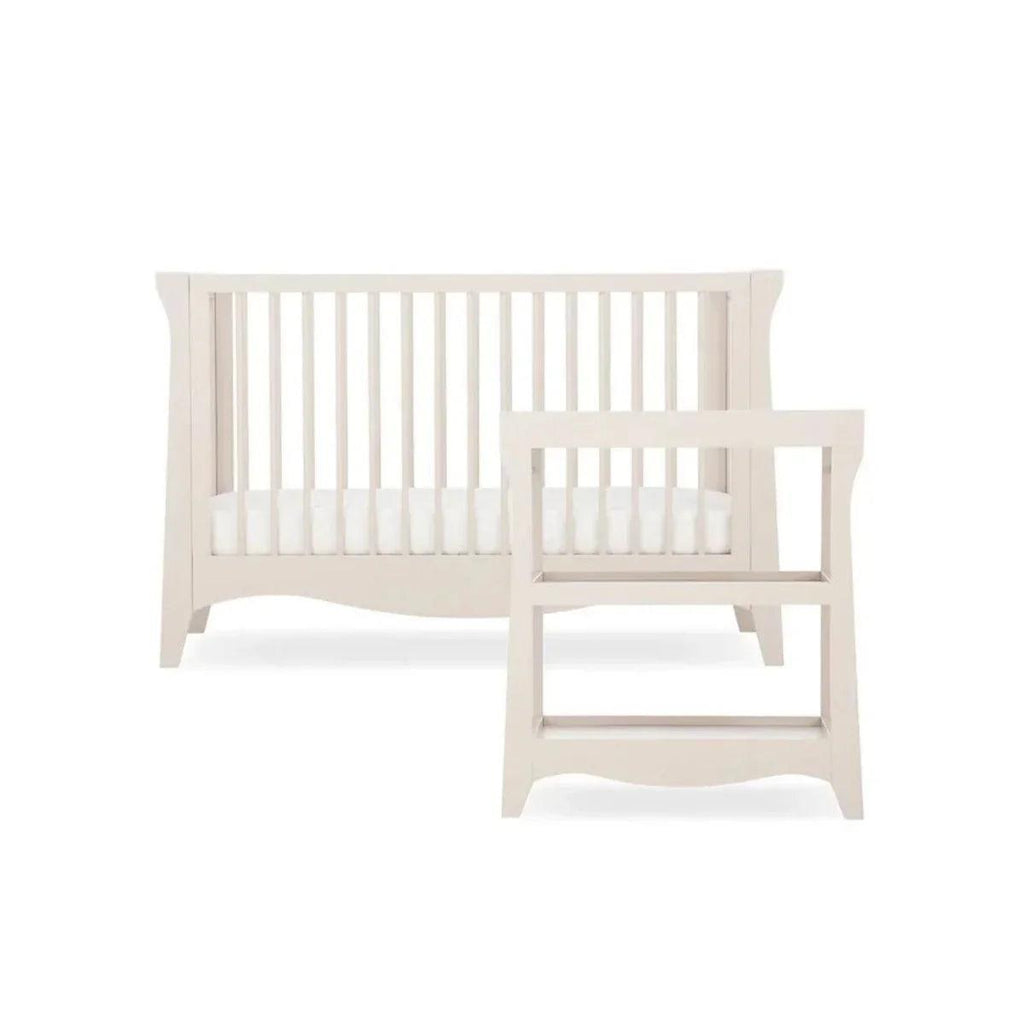 Cream nursery crib with white slats and open frame base, studio view