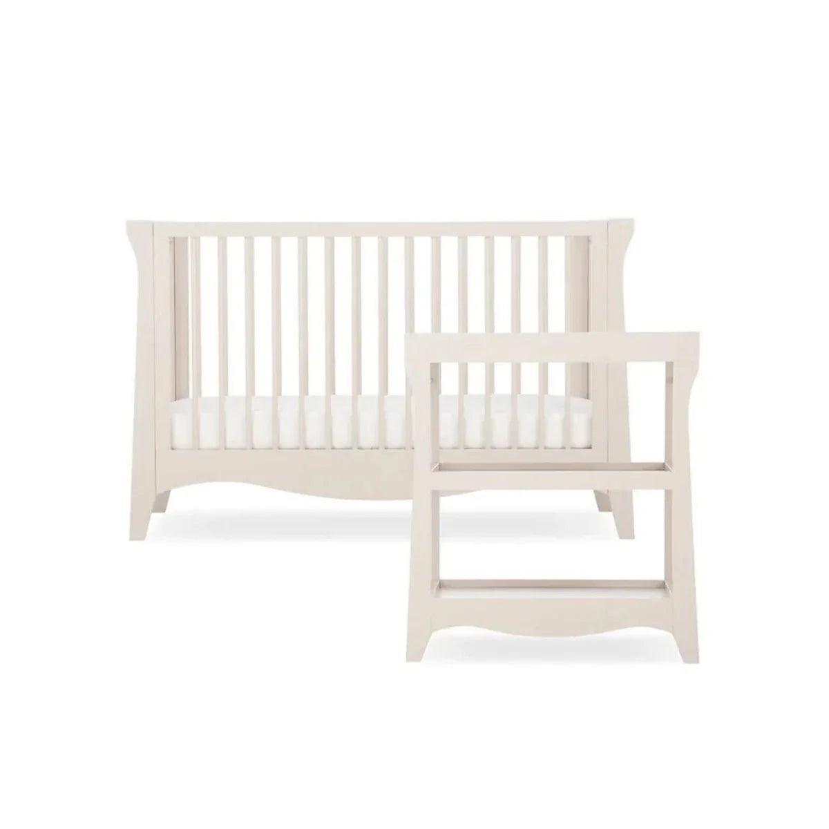 Cream nursery crib with white slats and open frame base, studio view