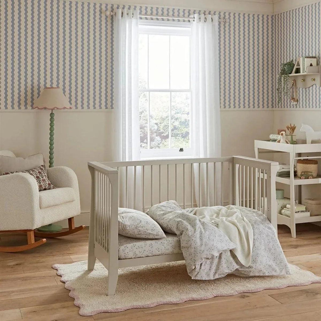 Cream nursery crib with quilted bedding and soft throw over the side