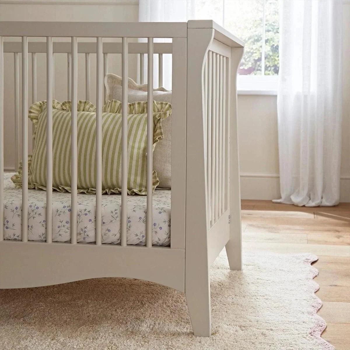 Cream crib side view with vertical slats and tucked green patterned pillow