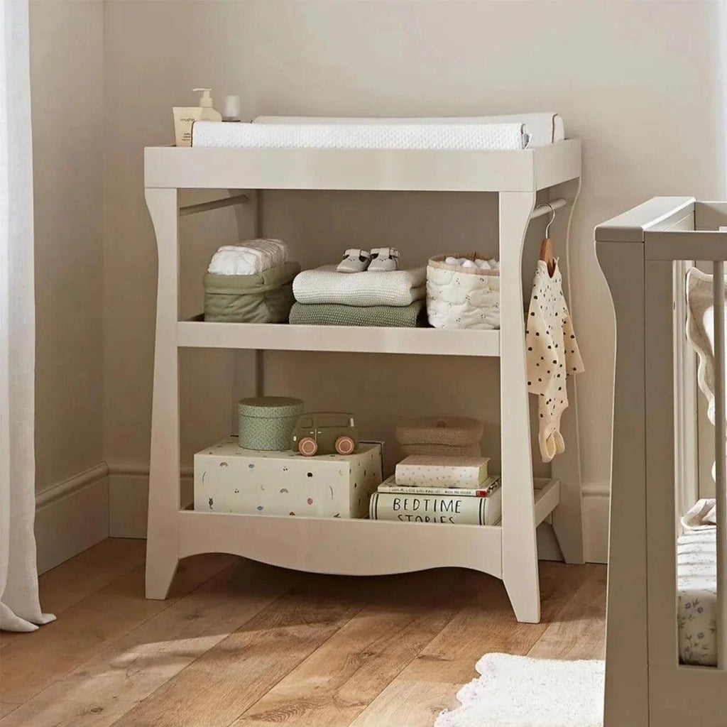 White changing table with open shelves, folded linens, and baby clothes on side