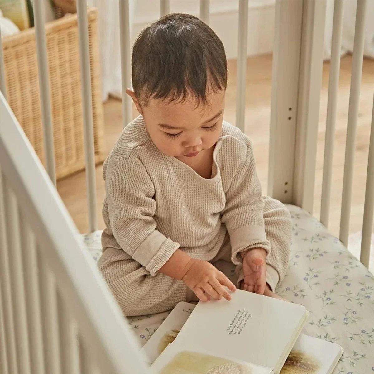 Toddler sitting inside a white mini cot bed with vertical rail sides