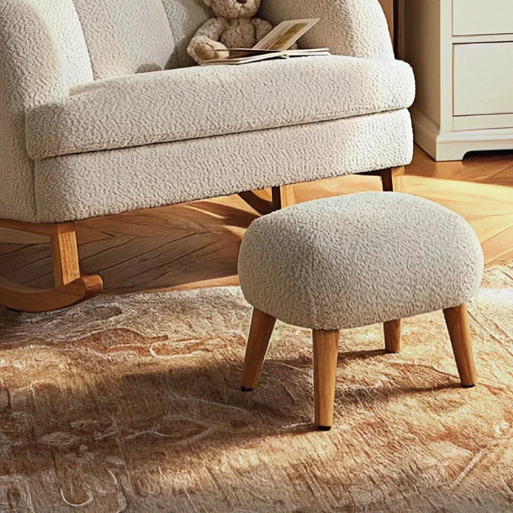 Light beige boucle foot stool with tapered wooden legs beside nursing chair