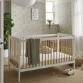 White and natural cot bed with vertical slats, raised sides, and grey fabric blanket.